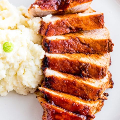 UPCLOSE PHOTO OF BROWN SUGAR PORK CHOP SLICED INTO 7 PIECES ON A WHITE PLATE NEXT TO A SIDE SERVING OF MASHED POTATOES