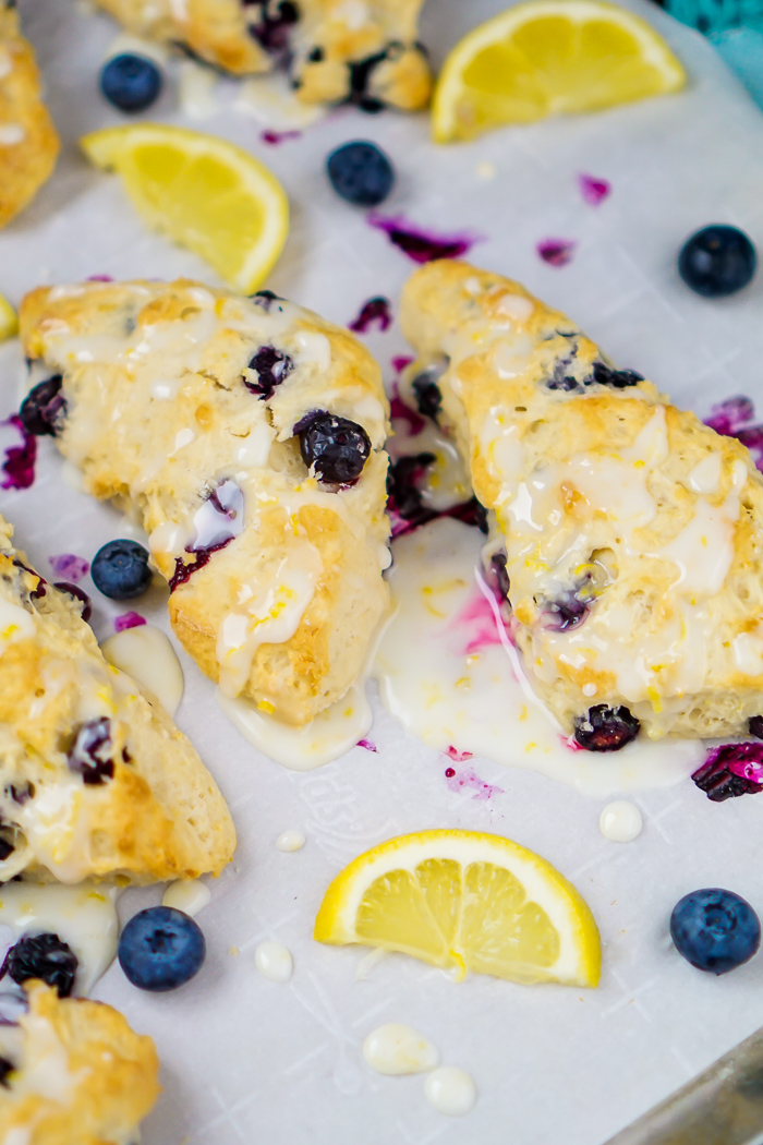 Lemon and Blueberry Scones with a delicious lemon glaze drizzled on top and pooled around the scones on the parchment paper. 
