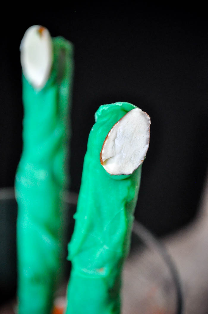 up close shot of a pretzel rod dipped in dark green candy melts with an almond slice at the end to make it look like a monster finger for a halloween treat