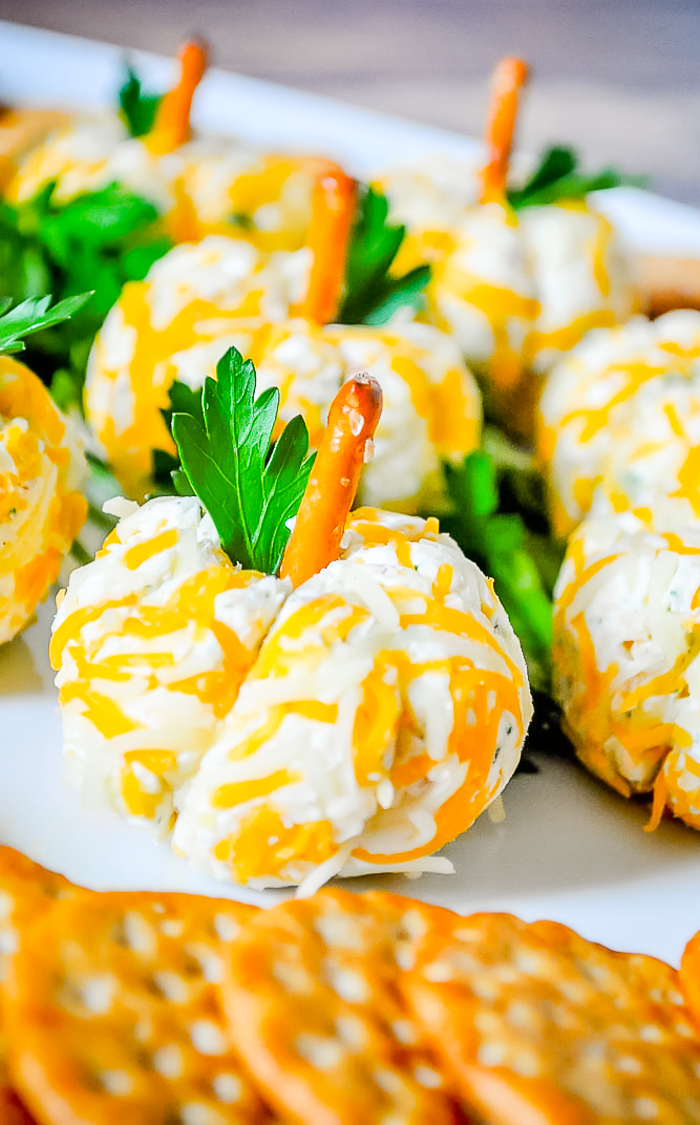 up close photo of a white plate filled with pumpkin shaped cheese balls with pretzel stem.