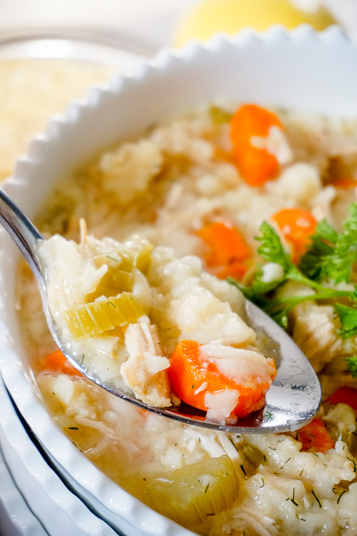 A stack of three white bowls is in frame close up with the top bowl willed with lemon chicken orzo soup. A spoon rests on the bowl and is filled with chunks of carrot, celery, chicken and orzo pasta. 