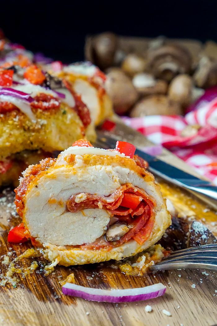 Stuffed Pizza Chicken Roll up is shown cut in half to reveal the roll of the chicken with pepperoni, chopped mushrooms, tomatoes, and marinara sauce in the middle. 