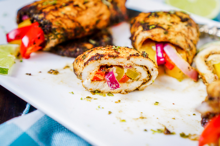 Baked Fajita Chicken Roll Ups stuffed with bell peppers and red onions and topped with lime zest are cut open to reveal middle and are sitting on a white plate
