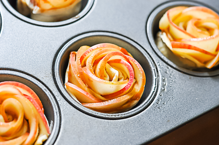 muffin pan with unbaked apple pastries that show apple slices in a pretty rose shape