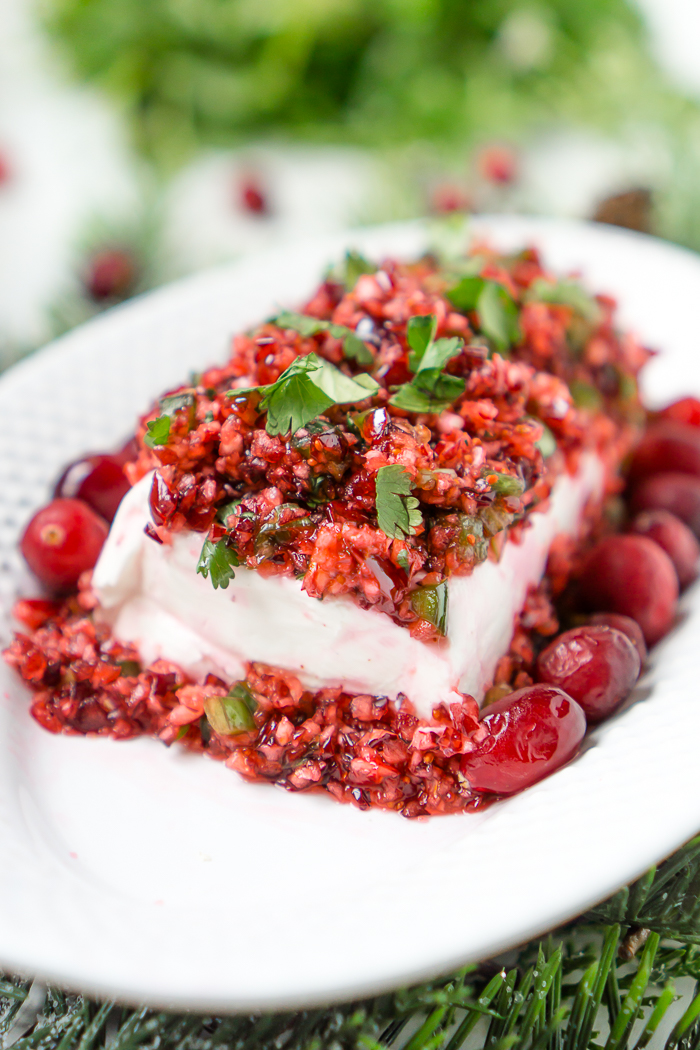 close up photo of a diced cranberry and jalapeno dip poured onto a block of cream cheese with chopped cilantro on top as garnish