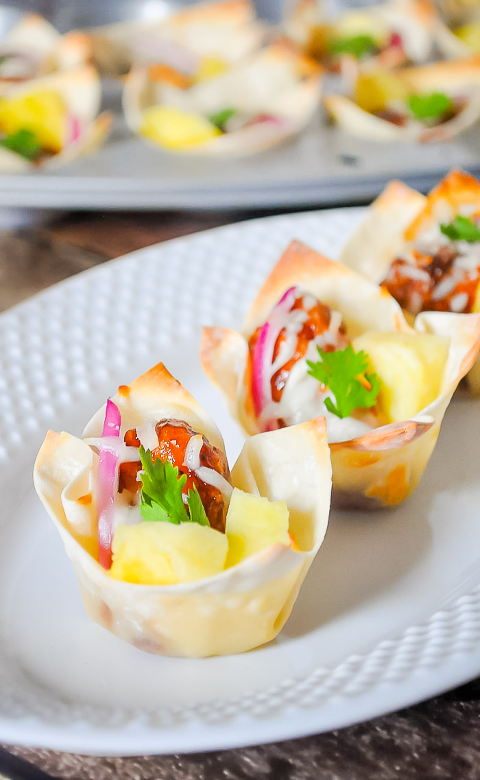 Hawaiian BBQ Chicken Cups is the perfect party food!! Use wonton sheets to make baked wonton cups you can fill with bbq boneless chicken wings, pineapple, onions, cheese and cilantro. Sweet and savory!