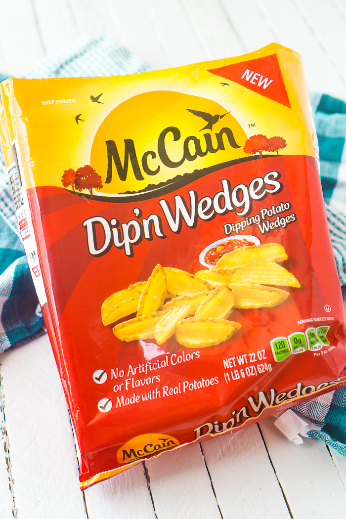 McCain Dip'n Wedges yellow and red bag sitting on a teal plaid napkin and white plank wood