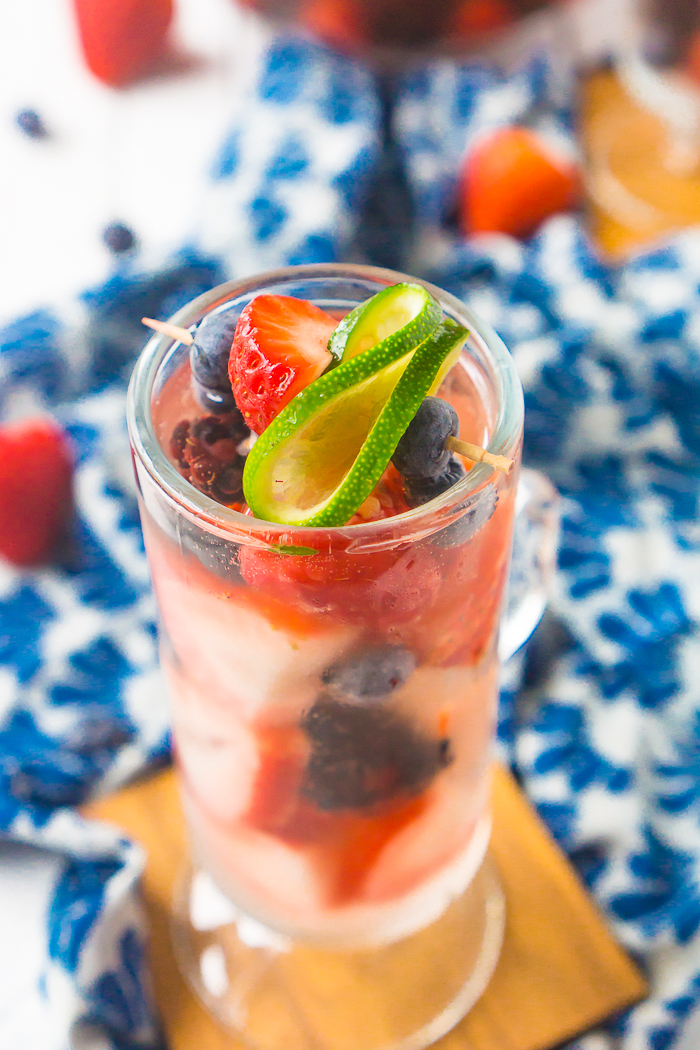 A white wine sangria filled with strawberries, blueberries, blackberries and raspberries is topped off with a berry and curled lime slice on a toothpick. 
