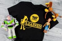 Toy Story Land SVG with Woody is ironed onto black tshirt with heat transfer vinyl as a Disney World Shirt with Slinky Mickey Ears and Woody and Buzz action figures sitting by the shirt.