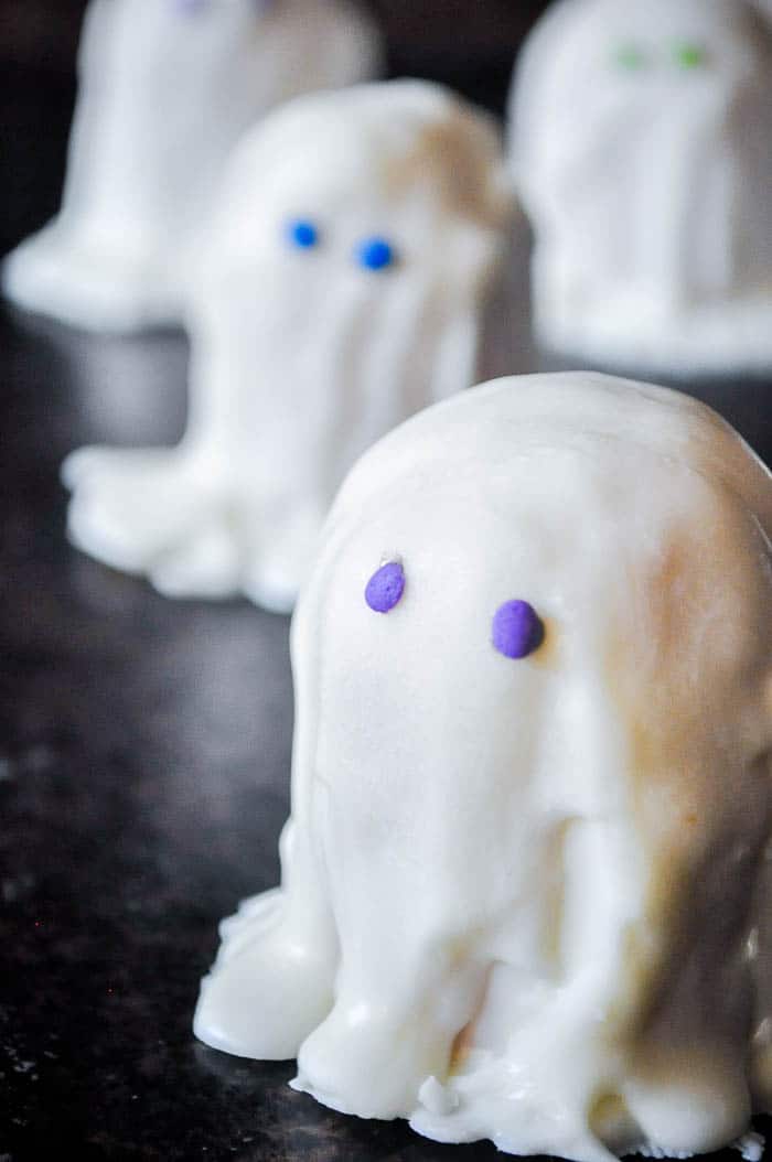 Up close shot of vanilla coating poured on and draped around the bottom of a halved twinkie to look like a ghost with purple candy eyes